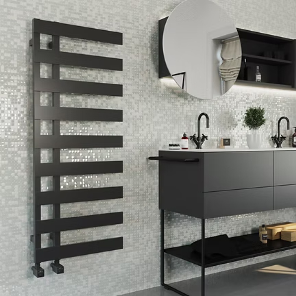 Lifestyle image of the Radox Dora 1250mm x 500mm Matt Black Heated Towel Rail mounted on a wall next to a basin and round mirror